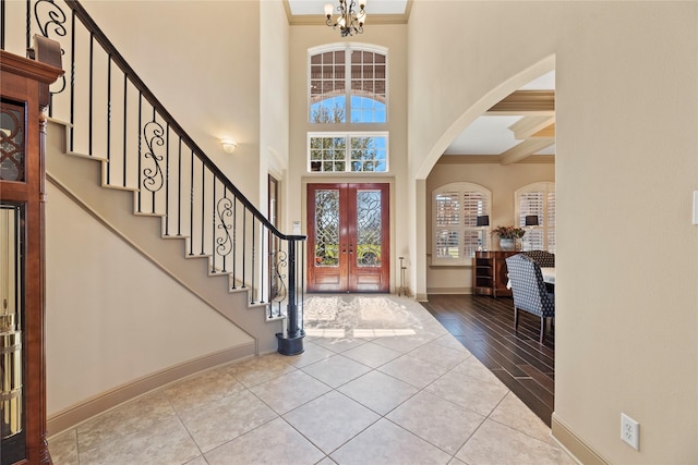 foyer entrance with tile patterned flooring, a chandelier, stairway, ornamental molding, and french doors