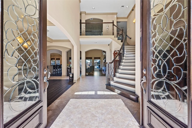 tiled foyer featuring ornamental molding, stairway, arched walkways, baseboards, and a towering ceiling