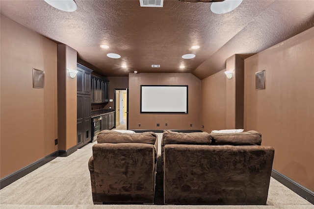 home theater room featuring visible vents, light carpet, a textured ceiling, and baseboards