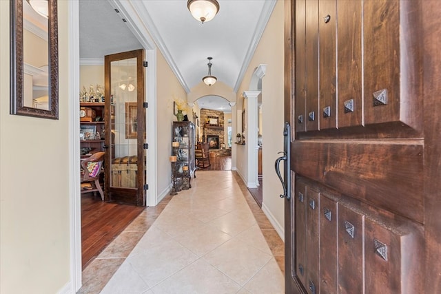 entrance foyer featuring light tile patterned floors, baseboards, decorative columns, ornamental molding, and a stone fireplace