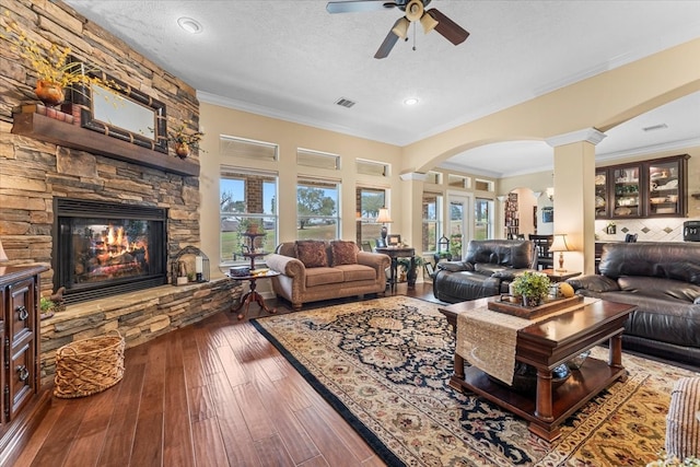 living room featuring visible vents, ornamental molding, a stone fireplace, hardwood / wood-style flooring, and ornate columns