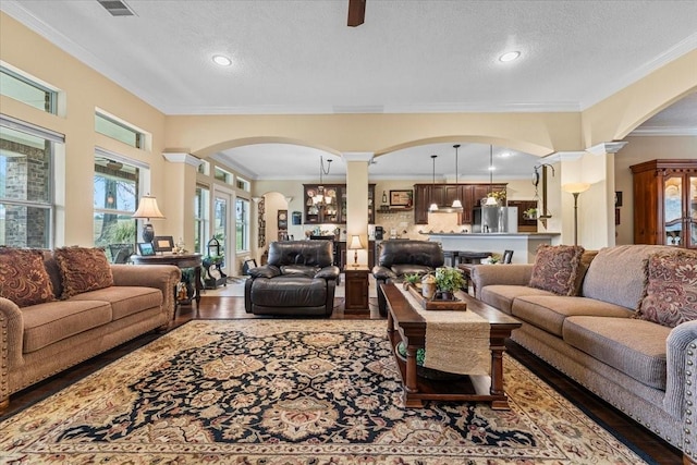 living room featuring decorative columns, a textured ceiling, wood finished floors, and ornamental molding