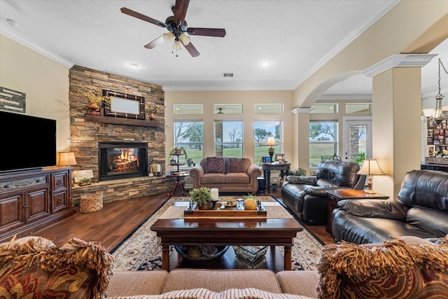 living area featuring wood finished floors, visible vents, ornate columns, a stone fireplace, and crown molding