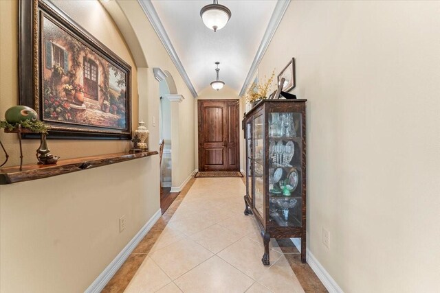 corridor featuring crown molding, light tile patterned floors, arched walkways, and baseboards