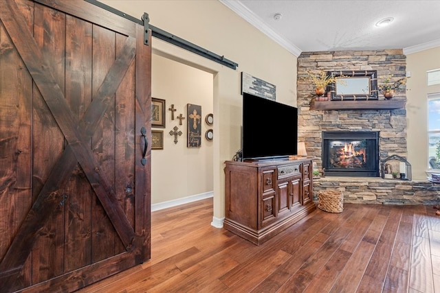 living area with ornamental molding, wood finished floors, a barn door, a stone fireplace, and baseboards