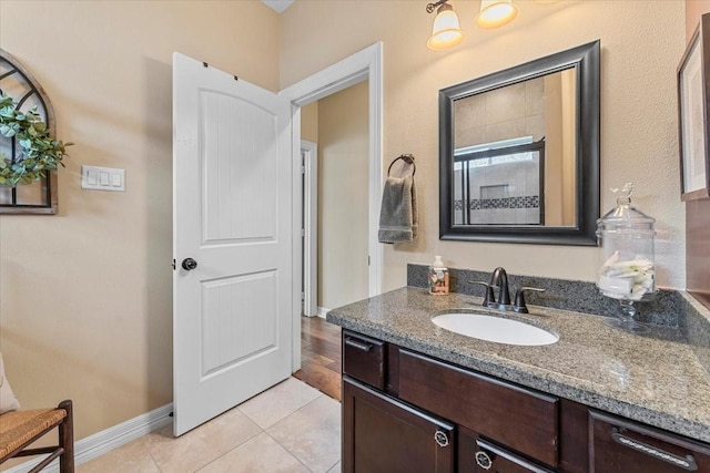 full bath with baseboards, walk in shower, vanity, and tile patterned flooring