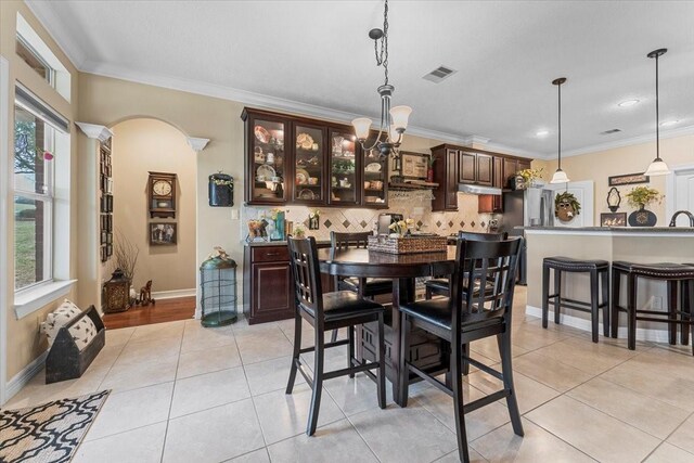 dining room with visible vents, baseboards, ornamental molding, light tile patterned floors, and arched walkways