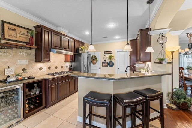 kitchen with under cabinet range hood, crown molding, beverage cooler, and appliances with stainless steel finishes