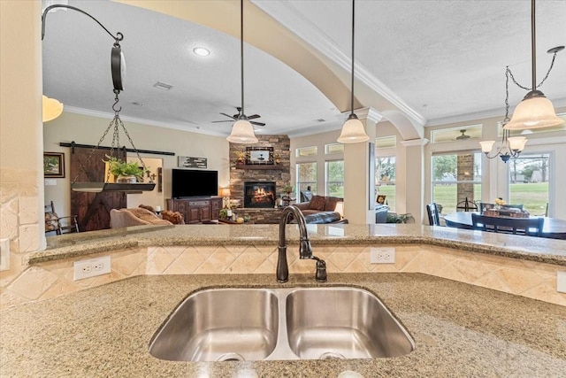 kitchen with a textured ceiling, a fireplace, light stone countertops, and a sink