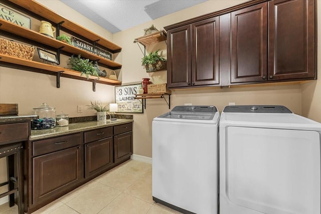 laundry area with washer and clothes dryer, a textured ceiling, cabinet space, light tile patterned floors, and baseboards