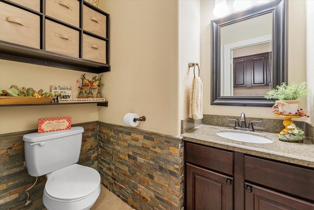 half bathroom with vanity, toilet, and wainscoting