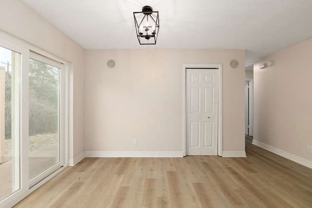 unfurnished dining area featuring an inviting chandelier, baseboards, and light wood-style floors