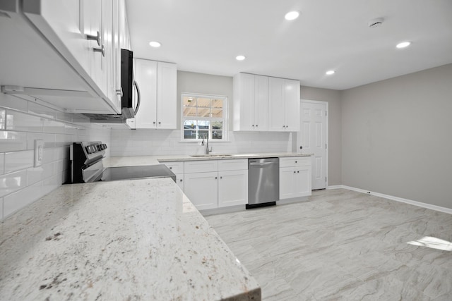 kitchen with backsplash, light stone countertops, appliances with stainless steel finishes, white cabinets, and a sink