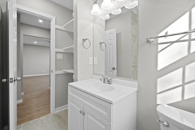 bathroom featuring baseboards, toilet, wood finished floors, and vanity