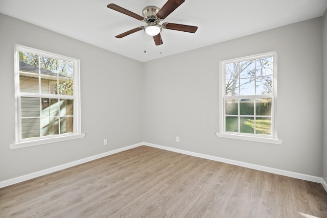 empty room featuring a wealth of natural light, a ceiling fan, light wood-style floors, and baseboards