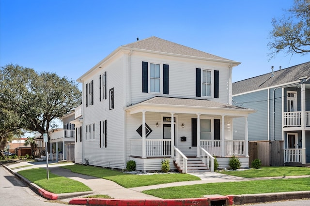 american foursquare style home with a porch, a front yard, and a shingled roof