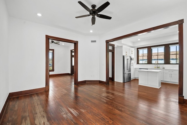 unfurnished living room featuring recessed lighting, baseboards, dark wood-type flooring, and a sink