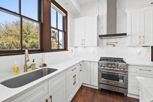 kitchen with a sink, dark wood-style floors, stainless steel stove, white cabinets, and wall chimney range hood