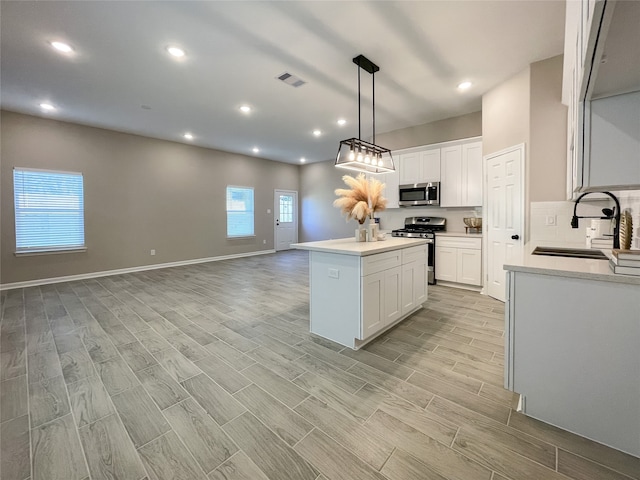 kitchen with visible vents, wood tiled floor, a sink, stainless steel appliances, and a center island