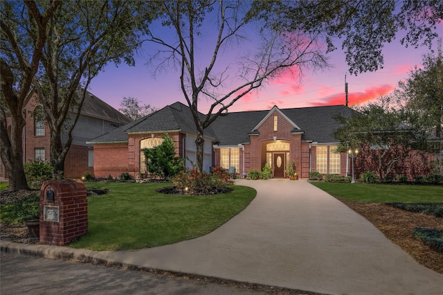 view of front of house featuring a yard, an attached garage, a shingled roof, concrete driveway, and brick siding