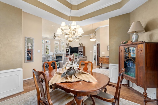 dining space featuring crown molding, a fireplace, light wood finished floors, and wainscoting