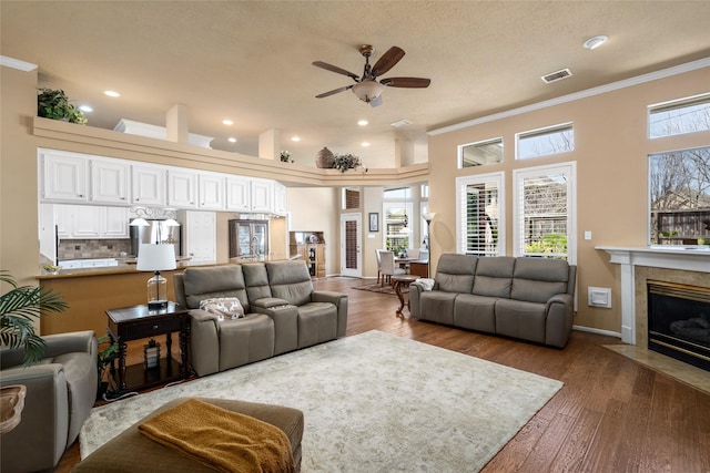 living area with wood finished floors, visible vents, a fireplace, ceiling fan, and ornamental molding