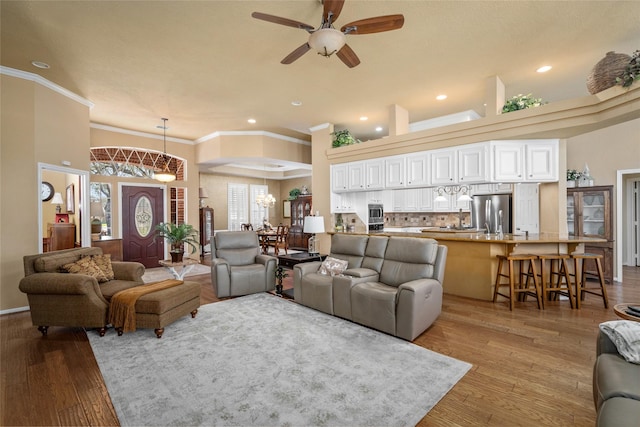 living room with recessed lighting, a towering ceiling, crown molding, ceiling fan with notable chandelier, and light wood-type flooring