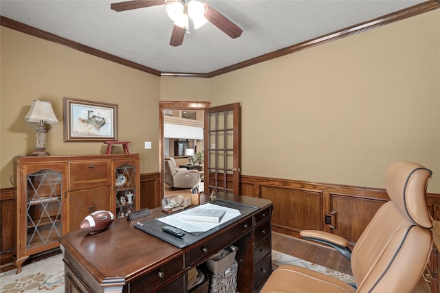 office area featuring ceiling fan, a wainscoted wall, ornamental molding, light wood-style flooring, and a textured ceiling