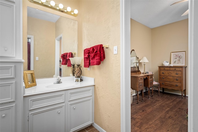 bathroom with vanity, wood finished floors, baseboards, and a textured wall