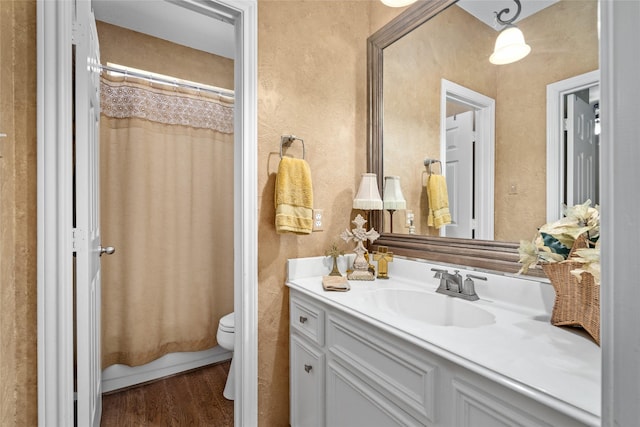 bathroom with toilet, vanity, a textured wall, and wood finished floors