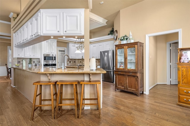 kitchen featuring decorative backsplash, appliances with stainless steel finishes, wood finished floors, white cabinets, and a sink