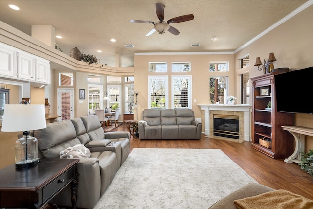 living room with a tiled fireplace, visible vents, crown molding, and wood finished floors