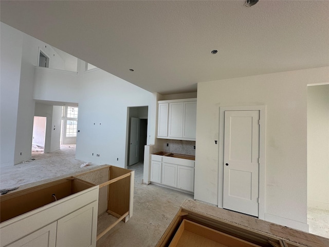 kitchen with white cabinets, concrete flooring, and a towering ceiling