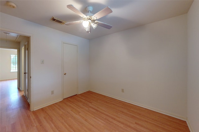 unfurnished room with visible vents, light wood-style flooring, a ceiling fan, baseboards, and attic access