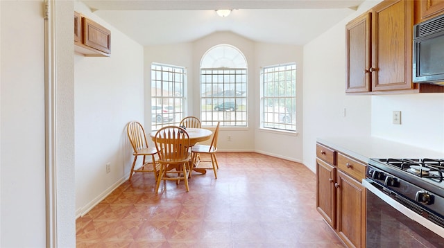 kitchen featuring gas range, brown cabinets, black microwave, and vaulted ceiling