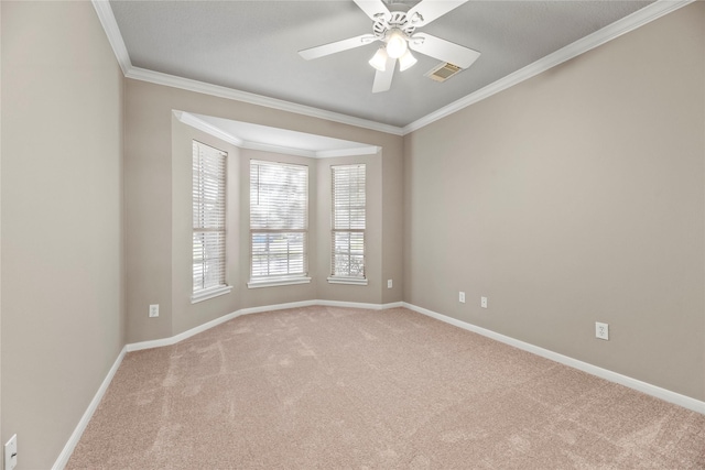 carpeted spare room with ceiling fan, visible vents, baseboards, and ornamental molding