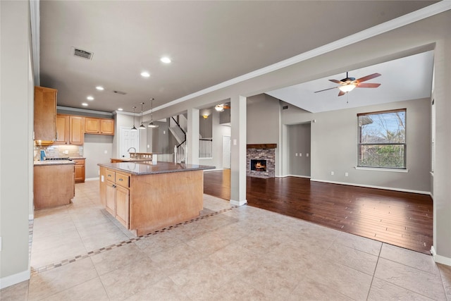 kitchen with visible vents, an island with sink, backsplash, open floor plan, and a brick fireplace