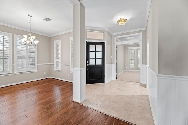 entrance foyer featuring visible vents, crown molding, a chandelier, a wainscoted wall, and hardwood / wood-style floors