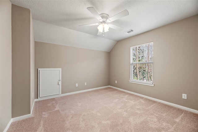 spare room featuring baseboards, lofted ceiling, a textured ceiling, and light carpet