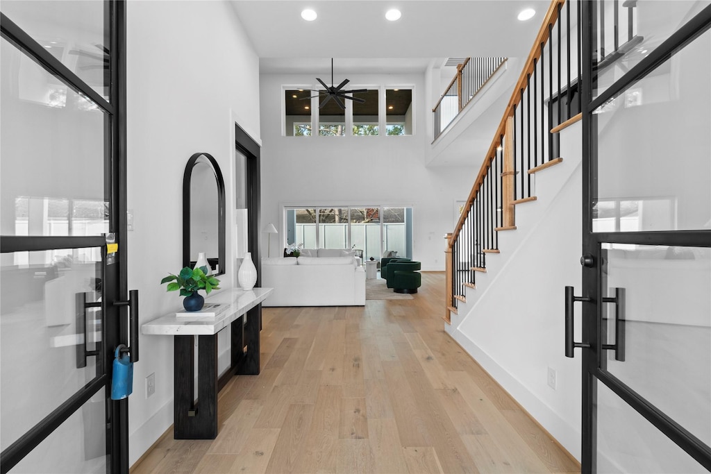 foyer with baseboards, stairs, light wood-type flooring, recessed lighting, and a towering ceiling