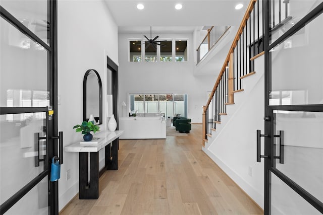 foyer with baseboards, stairs, light wood-type flooring, recessed lighting, and a towering ceiling