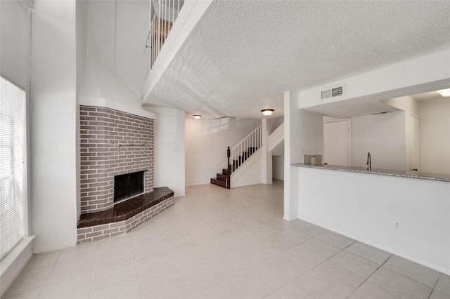 unfurnished living room featuring visible vents, light tile patterned flooring, a fireplace, stairs, and a textured ceiling