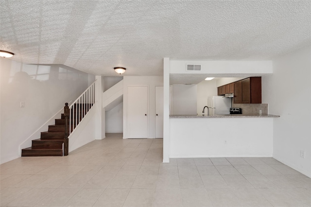 kitchen with visible vents, light stone counters, backsplash, a textured ceiling, and freestanding refrigerator