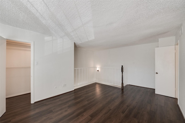 unfurnished bedroom with a walk in closet, a textured ceiling, a closet, and dark wood finished floors