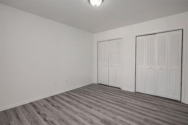 unfurnished bedroom with baseboards, multiple closets, and wood finished floors