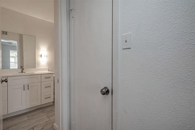 bathroom featuring wood finish floors, visible vents, vanity, and a textured wall