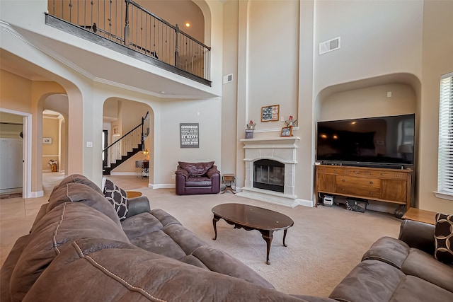 living area featuring visible vents, a high ceiling, a fireplace, arched walkways, and light carpet