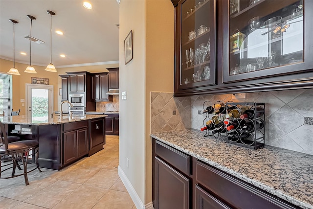 kitchen featuring light stone counters, light tile patterned floors, dark brown cabinetry, under cabinet range hood, and stainless steel microwave