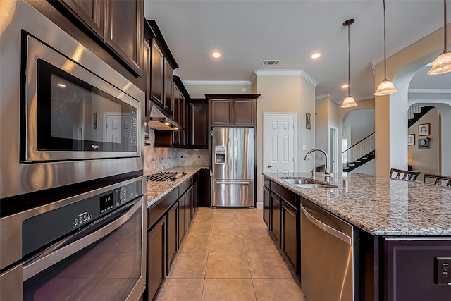 kitchen featuring dark brown cabinets, light tile patterned floors, appliances with stainless steel finishes, arched walkways, and a sink