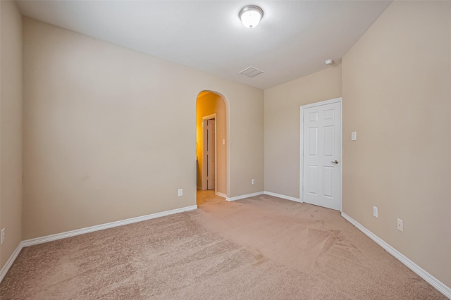 spare room with baseboards, arched walkways, and light carpet